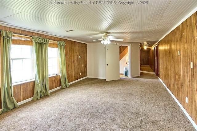 carpeted spare room with wooden walls, baseboards, and a ceiling fan