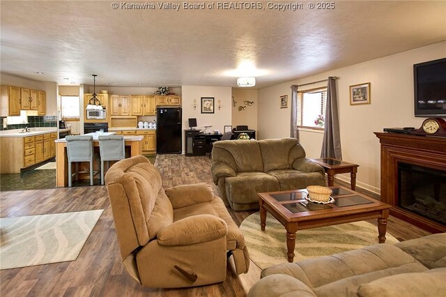 living area with a textured ceiling, a fireplace, baseboards, and dark wood-style flooring