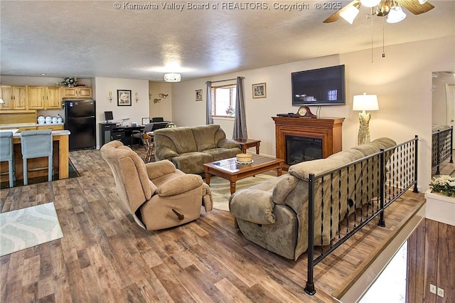 living room with ceiling fan, a textured ceiling, wood finished floors, and a glass covered fireplace