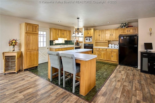 kitchen with black appliances, a kitchen island, light countertops, and dark wood-type flooring