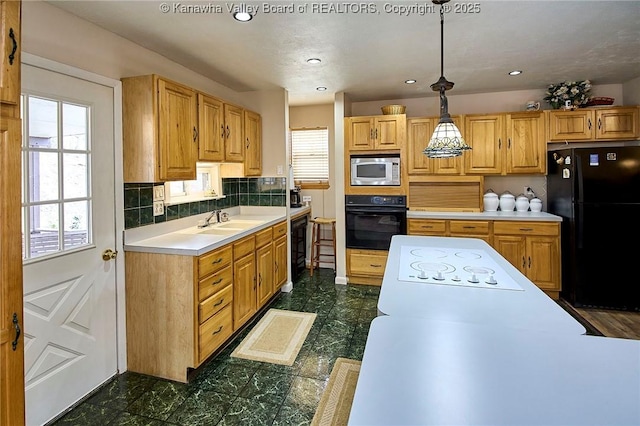 kitchen featuring decorative light fixtures, a sink, light countertops, black appliances, and backsplash