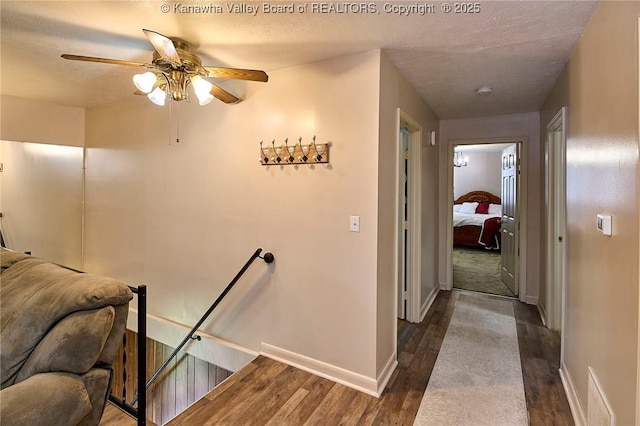 corridor featuring a textured ceiling, dark wood-type flooring, an upstairs landing, and baseboards