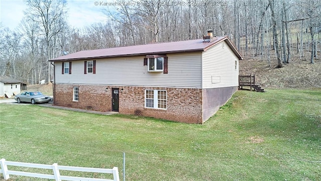 view of side of property with a yard, brick siding, a chimney, and fence