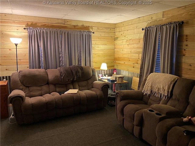 living area with carpet, wooden walls, and a drop ceiling