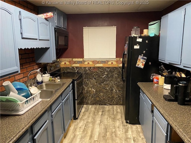 kitchen with dark countertops, black appliances, light wood finished floors, and a sink