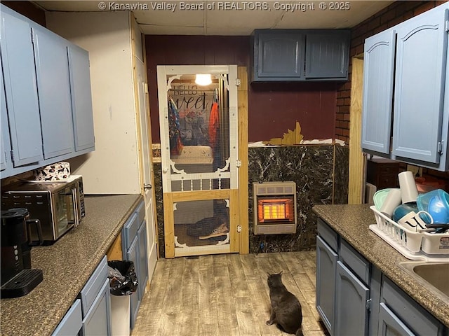 kitchen with light wood finished floors, heating unit, a paneled ceiling, gray cabinets, and a sink