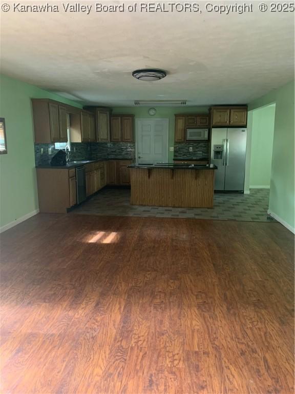 kitchen with white microwave, dark wood-style flooring, dishwasher, dark countertops, and stainless steel fridge