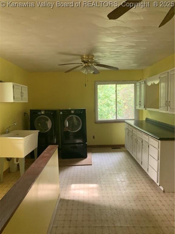 interior space featuring washing machine and clothes dryer, cabinet space, a ceiling fan, a sink, and baseboards