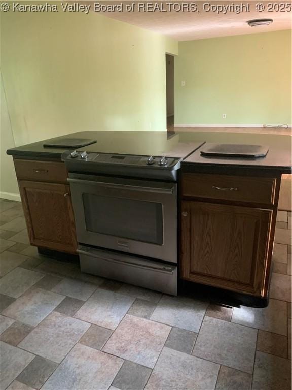 kitchen with dark countertops, electric stove, stone finish floor, and dark brown cabinets