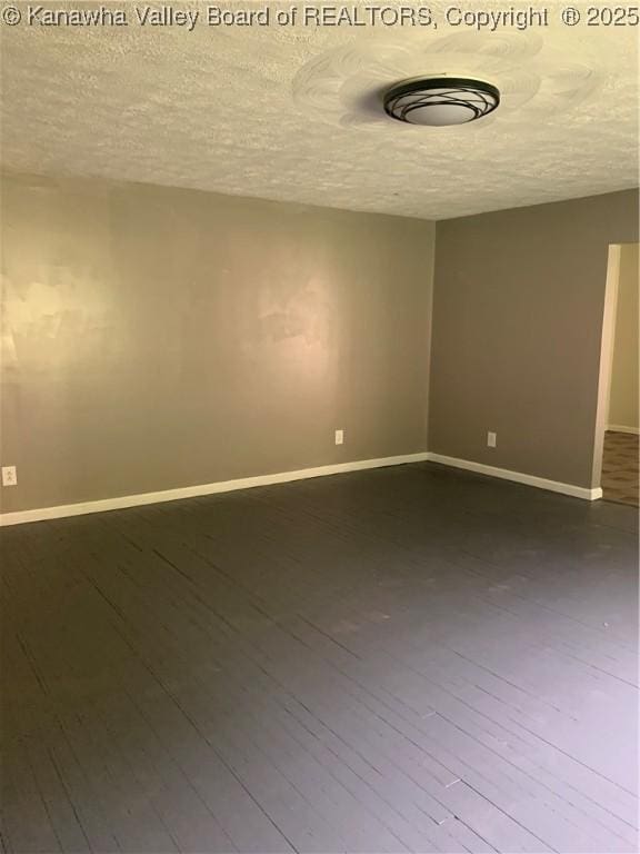 spare room with a textured ceiling, dark wood-type flooring, and baseboards