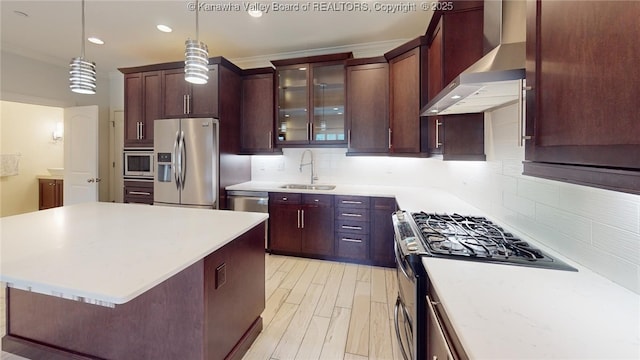 kitchen with appliances with stainless steel finishes, decorative light fixtures, light countertops, wall chimney range hood, and a sink