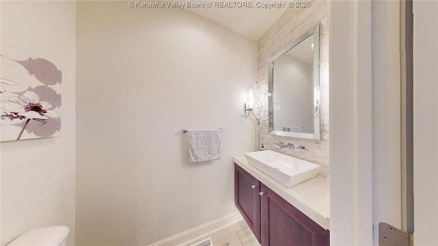 half bathroom featuring backsplash, baseboards, vanity, and toilet