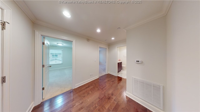 corridor with ornamental molding, baseboards, visible vents, and dark wood-type flooring