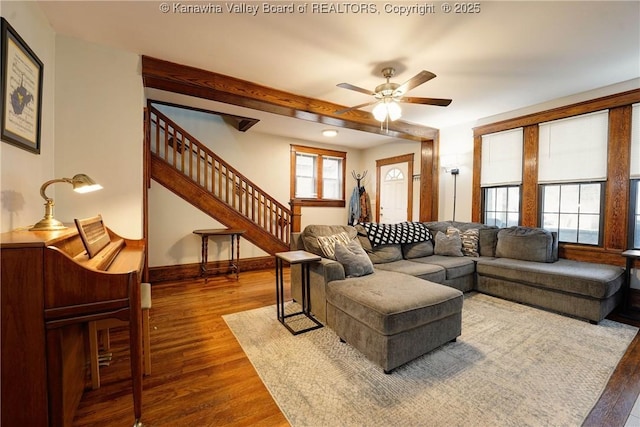 living area featuring stairway, wood finished floors, a ceiling fan, and a healthy amount of sunlight