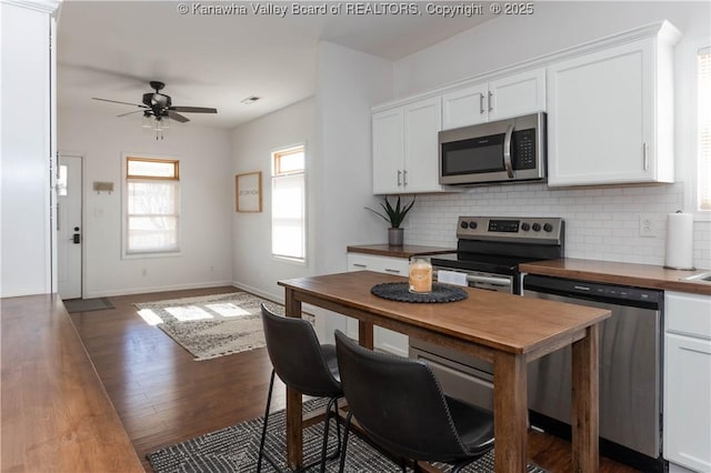 kitchen with white cabinets, butcher block counters, appliances with stainless steel finishes, and tasteful backsplash