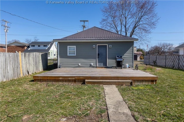 back of house featuring metal roof, fence, a deck, and a yard