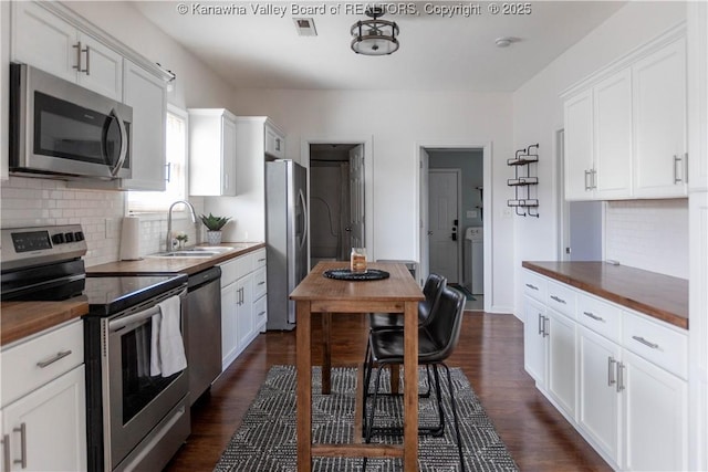 kitchen with dark wood-style flooring, a sink, white cabinets, appliances with stainless steel finishes, and washer / dryer