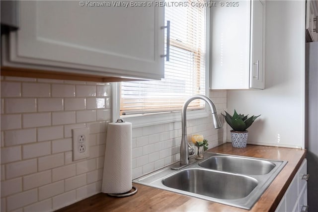 kitchen with butcher block counters, wood finished floors, a sink, white cabinets, and tasteful backsplash