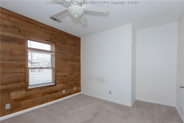 unfurnished room with wood walls, visible vents, a ceiling fan, and light colored carpet