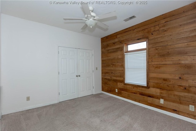 unfurnished bedroom featuring carpet, wooden walls, visible vents, and baseboards