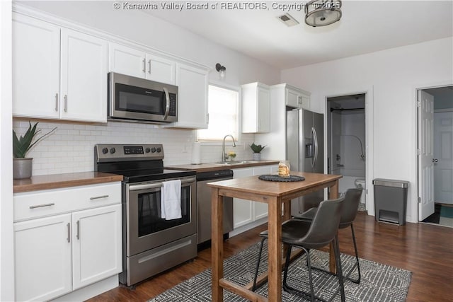 kitchen featuring appliances with stainless steel finishes, butcher block counters, white cabinetry, and a sink