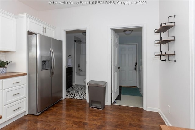 kitchen with dark wood-type flooring, stainless steel fridge, white cabinetry, and baseboards