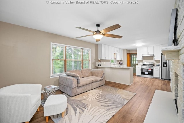 living area with baseboards, a ceiling fan, and light wood-style floors