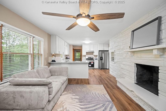 living room with a stone fireplace, wood finished floors, and a ceiling fan