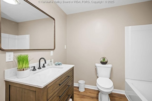 bathroom with vanity, wood finished floors, baseboards, toilet, and a bathtub