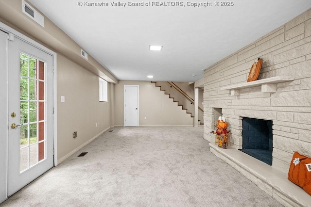 unfurnished living room featuring a stone fireplace, stairs, visible vents, and carpet floors