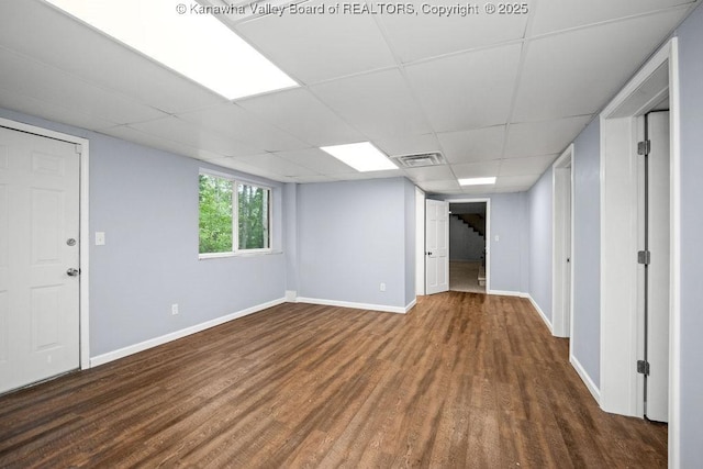 basement featuring a paneled ceiling, wood finished floors, visible vents, and baseboards