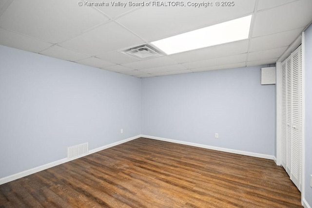 finished below grade area featuring visible vents, a paneled ceiling, baseboards, and wood finished floors