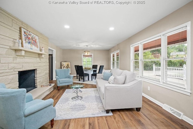 living room featuring visible vents, a stone fireplace, baseboards, and wood finished floors