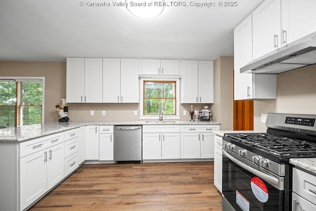 kitchen with a sink, under cabinet range hood, white cabinetry, appliances with stainless steel finishes, and a peninsula