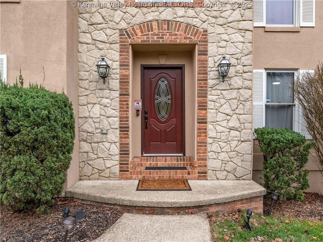 entrance to property featuring stucco siding, stone siding, and brick siding