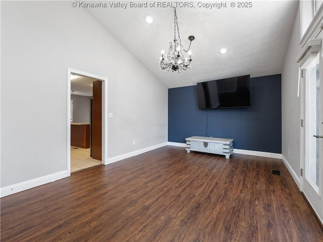 unfurnished living room with a notable chandelier, vaulted ceiling, baseboards, and wood finished floors