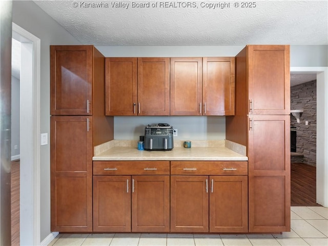 kitchen featuring light countertops, light tile patterned floors, brown cabinetry, and a textured ceiling