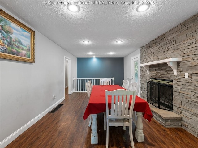 dining room with visible vents, a stone fireplace, baseboards, and wood finished floors