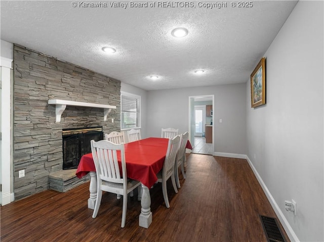 dining area featuring wood finished floors, baseboards, visible vents, a stone fireplace, and a textured ceiling