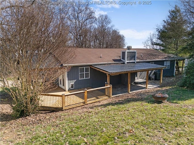 rear view of house with a lawn, a fire pit, metal roof, a wooden deck, and an attached carport