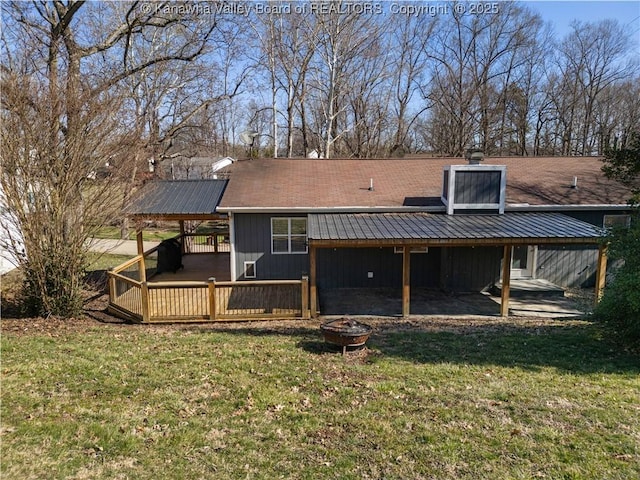 rear view of property with an attached carport, a wooden deck, a chimney, a fire pit, and a lawn