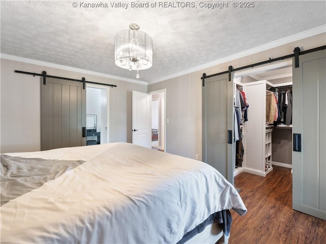 bedroom with dark wood-style floors, a spacious closet, crown molding, and a barn door