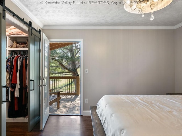 bedroom with a walk in closet, a barn door, ornamental molding, dark wood-style floors, and access to outside