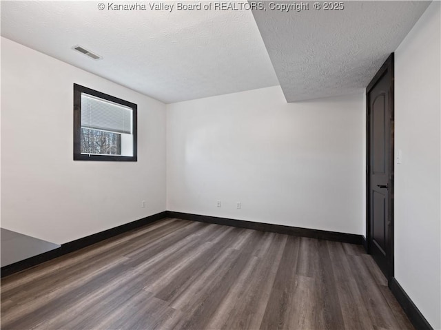 unfurnished room with visible vents, baseboards, dark wood-style flooring, and a textured ceiling