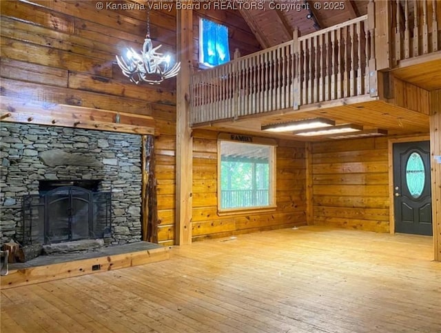 unfurnished living room featuring wooden walls, a fireplace, hardwood / wood-style flooring, a notable chandelier, and high vaulted ceiling