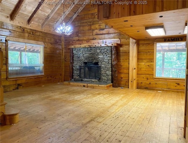 unfurnished living room with wooden walls, lofted ceiling with beams, wooden ceiling, a fireplace, and wood-type flooring