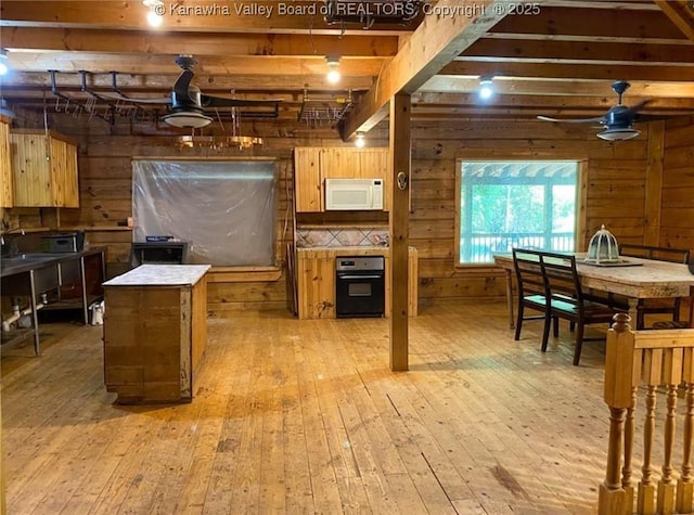 kitchen featuring light wood-type flooring, black oven, white microwave, and wooden walls