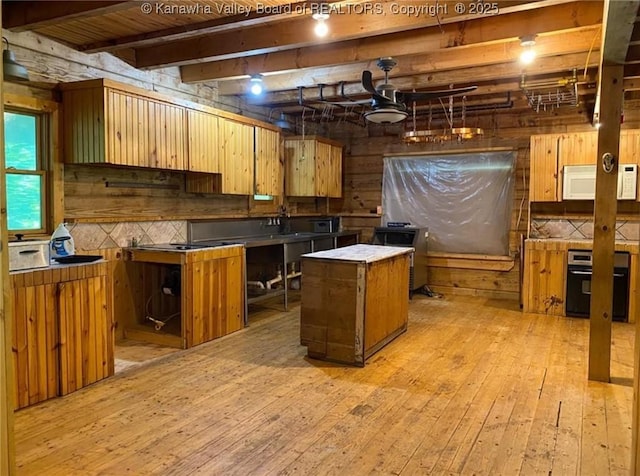 kitchen with light wood-type flooring, beamed ceiling, black oven, tasteful backsplash, and white microwave