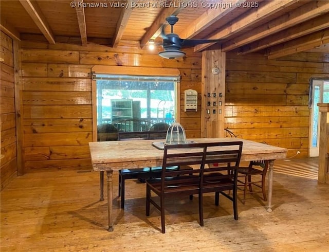 dining space with beam ceiling, wooden walls, light wood finished floors, and wooden ceiling