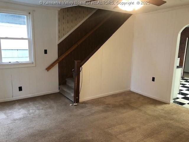 unfurnished living room featuring arched walkways, carpet flooring, and stairs